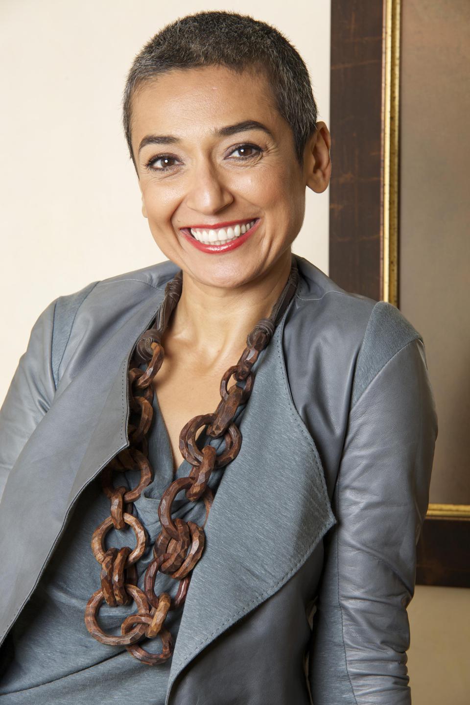 Portrait of a smiling woman, with a necklace and grey outfit.