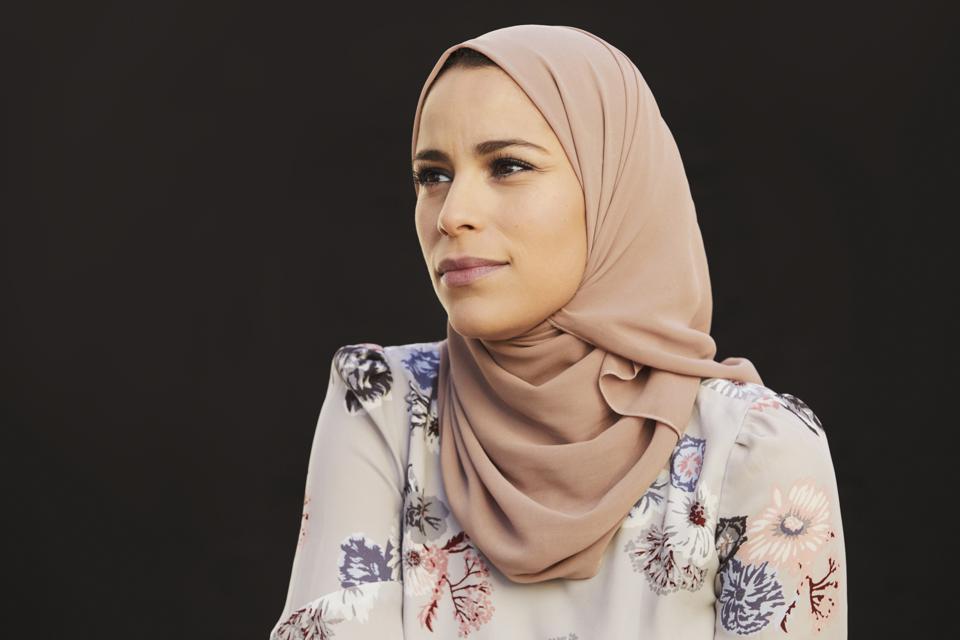 Portrait of Alaa Murabit, Libyan-Canadian woman, wearing a headscarf and a floral shirt.